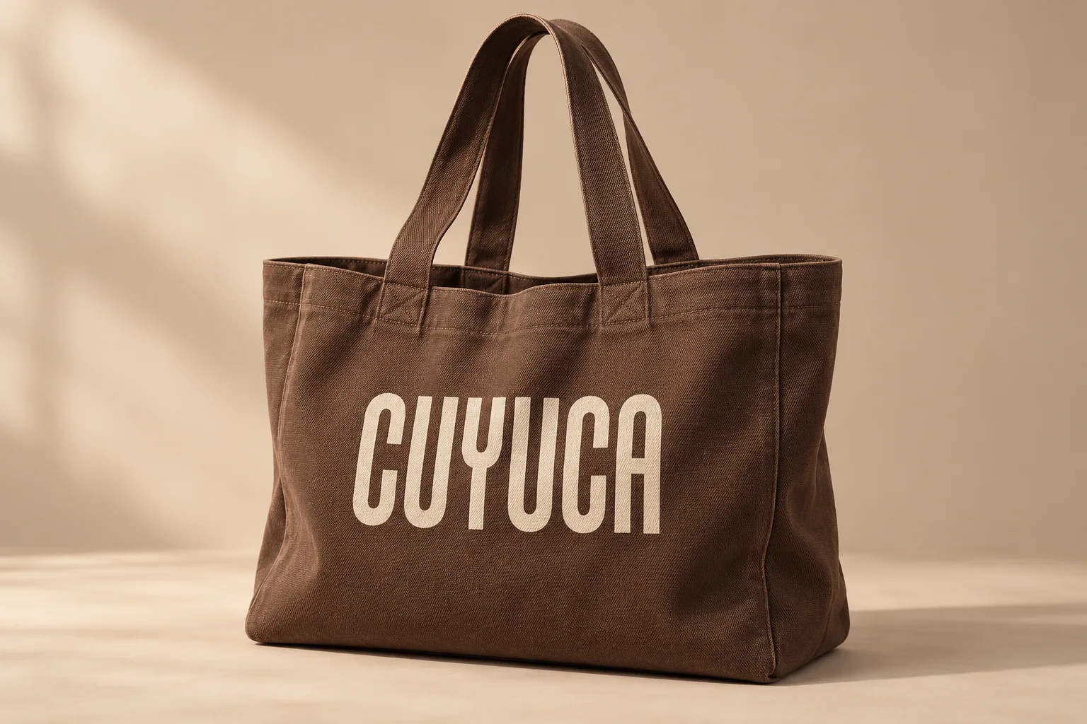 Cocoa-brown canvas tote printed with the solid Cuyuca wordmark in ivory.